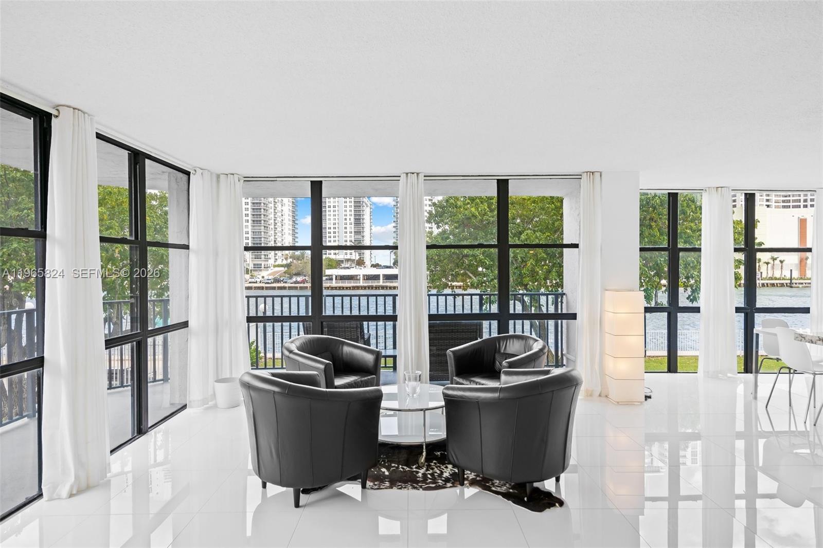 A bright living room features white tile floors, black leather chairs, and floor-to-ceiling windows — 800 Parkview Dr # 221, Hallandale Beach FL 33009, HALLANDALE BEACH, FL