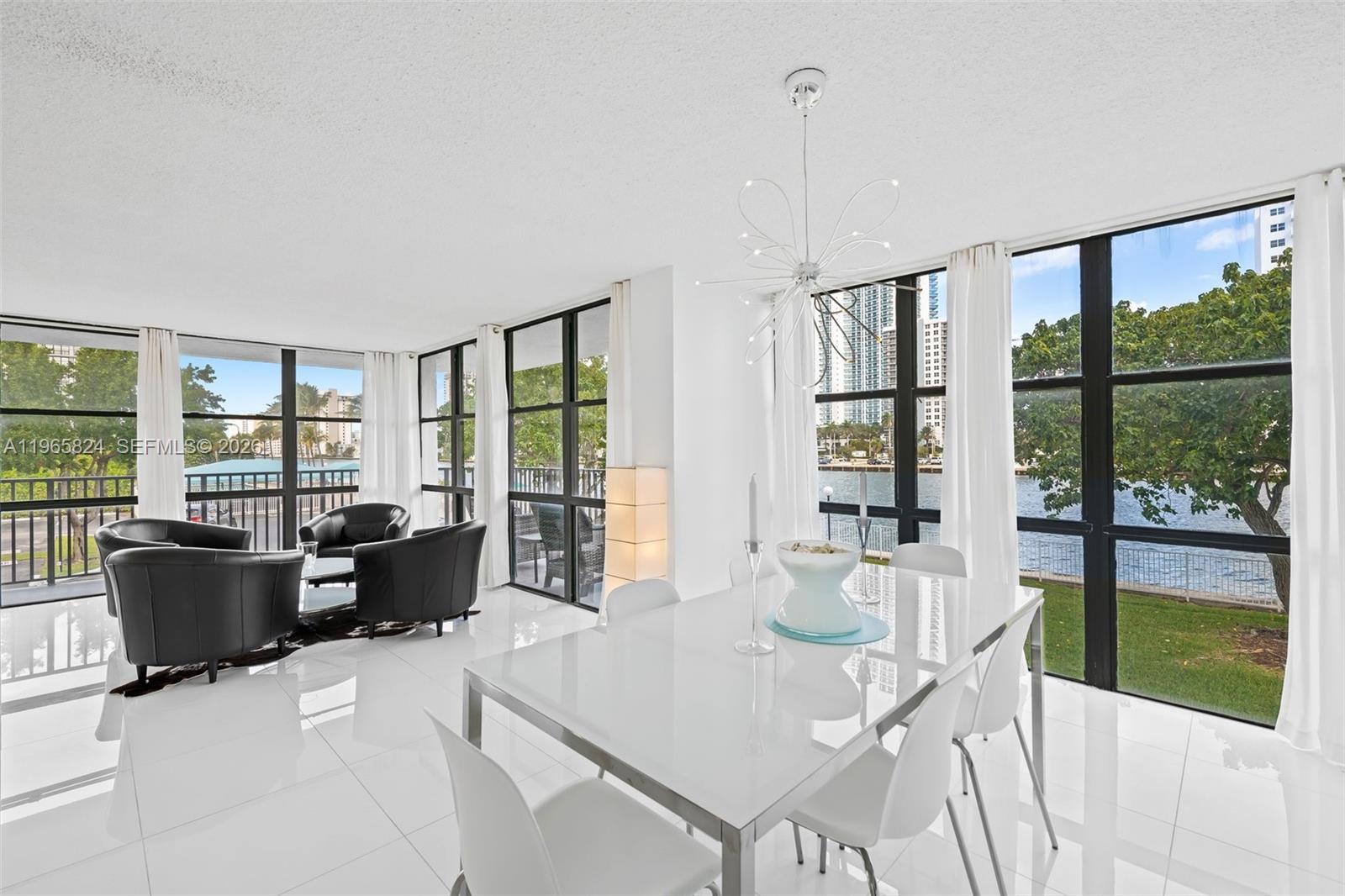 A bright dining and living area features white tile floors, floor-to-ceiling windows, and waterfront views — 800 Parkview Dr # 221, Hallandale Beach FL 33009, HALLANDALE BEACH, FL