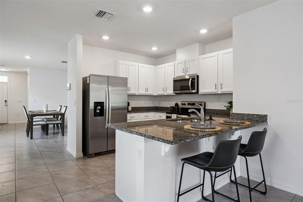A kitchen featuring white cabinets, granite countertops, stainless steel appliances, and a breakfast bar — 3624 SUNGROVE CIRCLE, SANFORD, FL