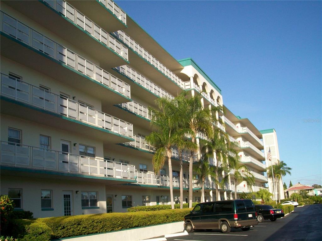 A multi-story apartment building with balconies and palm trees stands beside a parking lot — 2960 S 59TH STREET UNIT 311, GULFPORT, FL