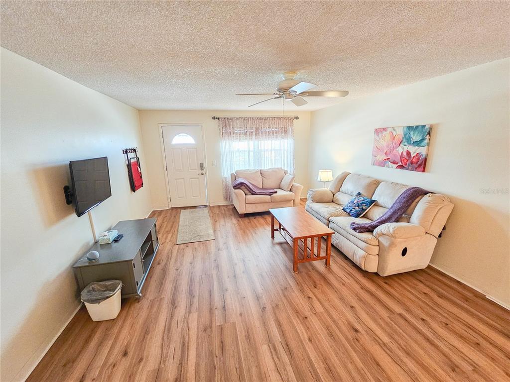 A living room features light wood-look flooring, a ceiling fan, and beige upholstered furniture — 2960 S 59TH STREET UNIT 311, GULFPORT, FL