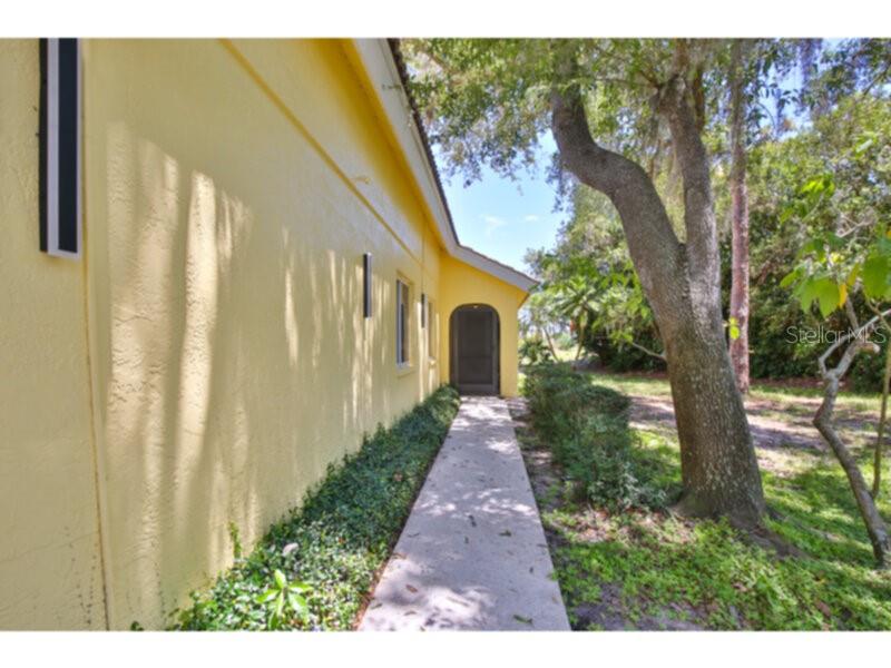 A yellow house exterior features a concrete walkway leading to a dark arched doorway — 4700 TIVOLI AVENUE, SARASOTA, FL