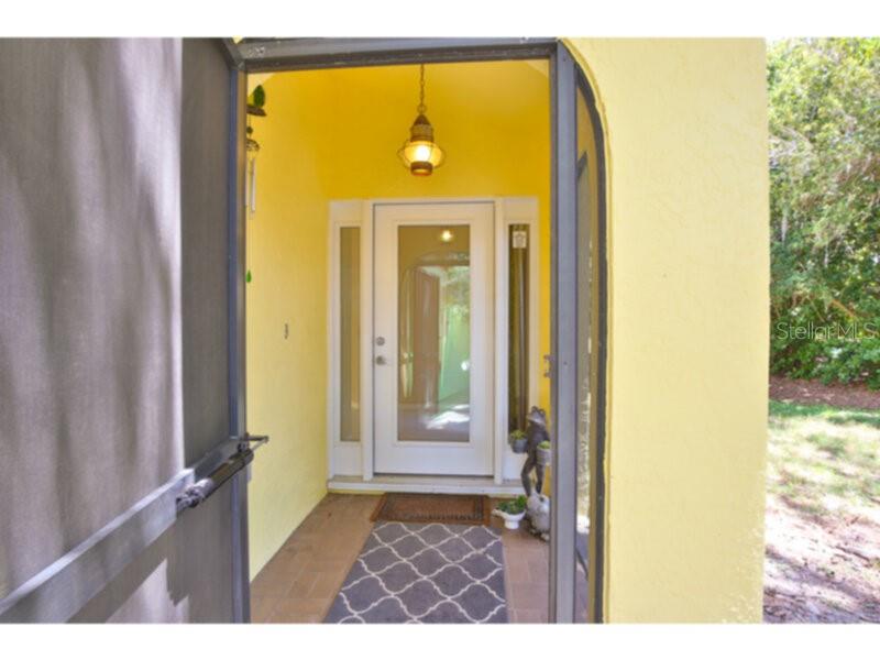 A view through a screen door into a yellow-walled entryway with a glass-paneled front door — 4700 TIVOLI AVENUE, SARASOTA, FL