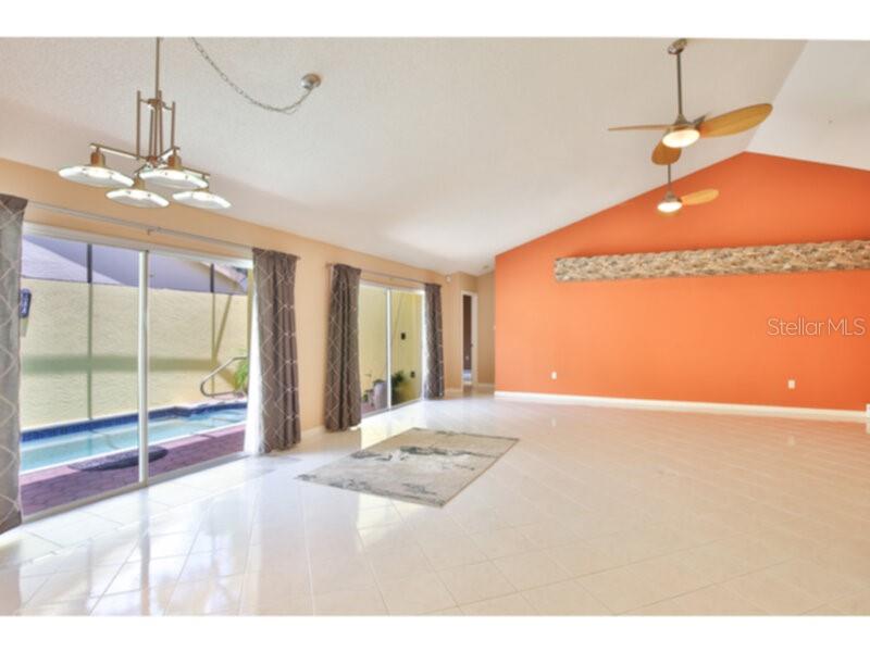 A bright living room features a vaulted ceiling, orange accent wall, and sliding glass doors — 4700 TIVOLI AVENUE, SARASOTA, FL