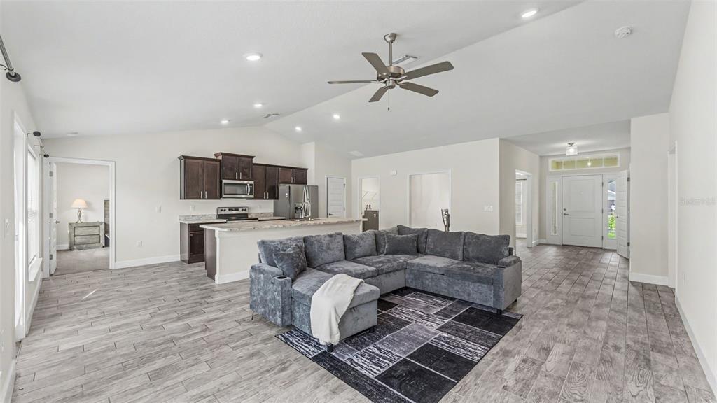 An open-concept living room and kitchen feature gray tile flooring and a sectional sofa — 314 ATHABASCA PLACE, POINCIANA, FL