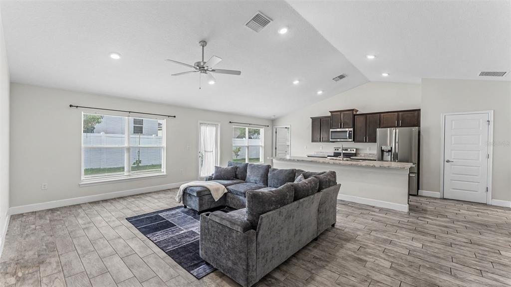 A living room with gray tile floors, a sectional sofa, and an open kitchen area — 314 ATHABASCA PLACE, POINCIANA, FL
