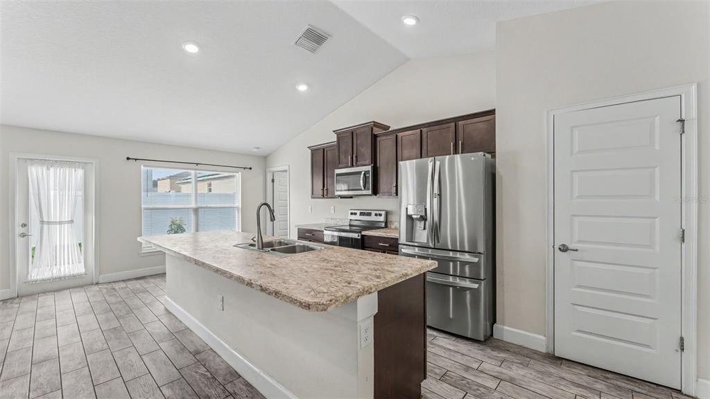 A kitchen features a large island, stainless steel appliances, dark wood cabinets, and tile flooring — 314 ATHABASCA PLACE, POINCIANA, FL