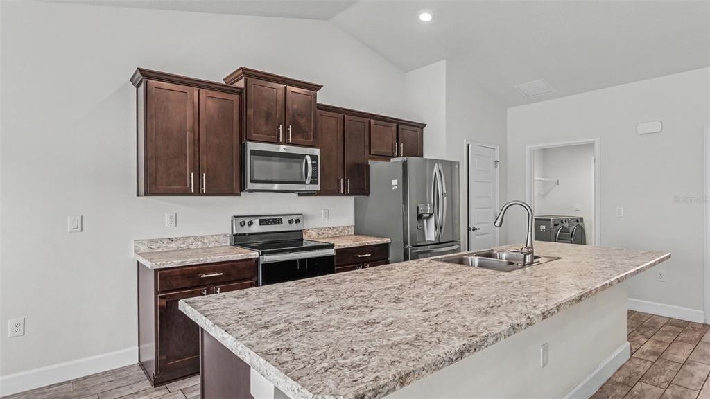 A kitchen features dark wood cabinets, stainless steel appliances, and a large stone-look island — 314 ATHABASCA PLACE, POINCIANA, FL