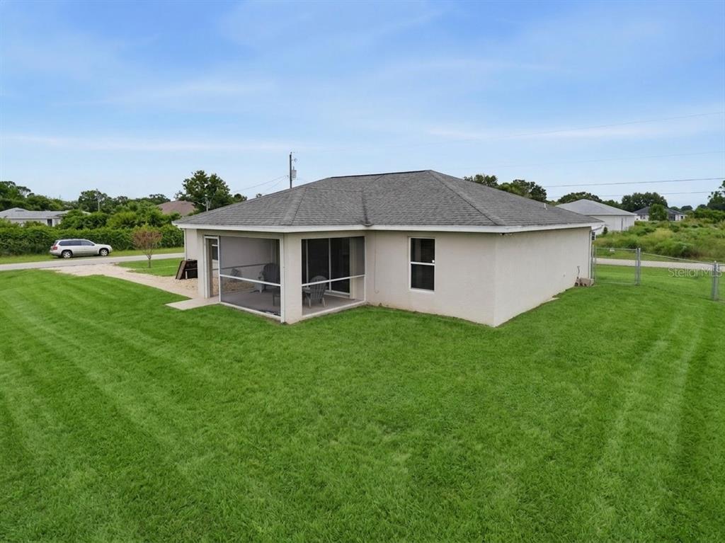 A rear view of a single-story house with a screened-in patio and a large lawn — 3109 64TH STREET W, LEHIGH ACRES, FL