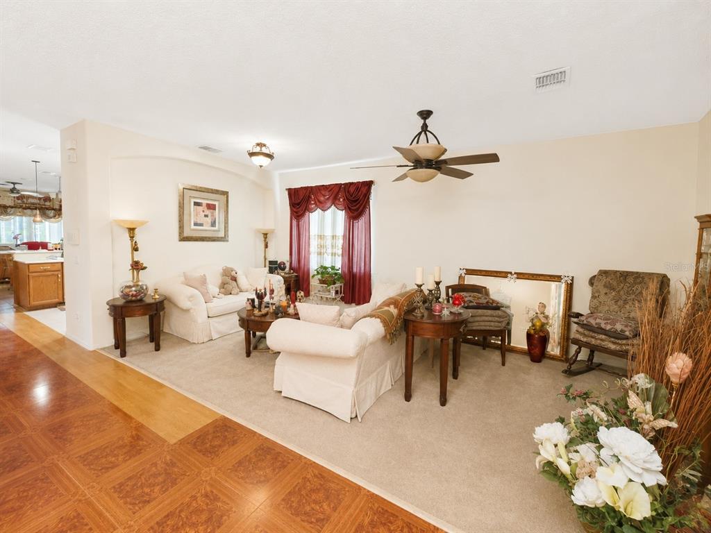 A living room with beige carpet, white sofas, a ceiling fan, and wood-look tile flooring — 9305 MANDRAKE COURT, TAMPA, FL