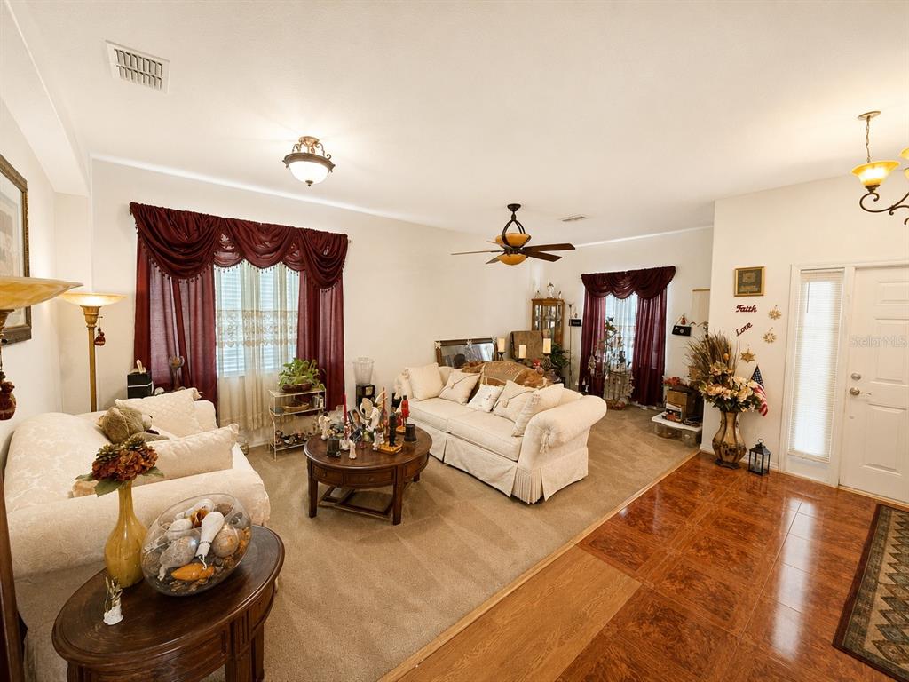 A living room features beige carpet, cream-colored sofas, dark wood furniture, and burgundy window treatments — 9305 MANDRAKE COURT, TAMPA, FL