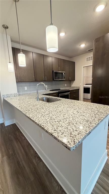 A kitchen features dark wood cabinets, granite countertops, a stainless steel sink, and pendant lighting — 530 ACADEMY DRIVE UNIT 201, KISSIMMEE, FL