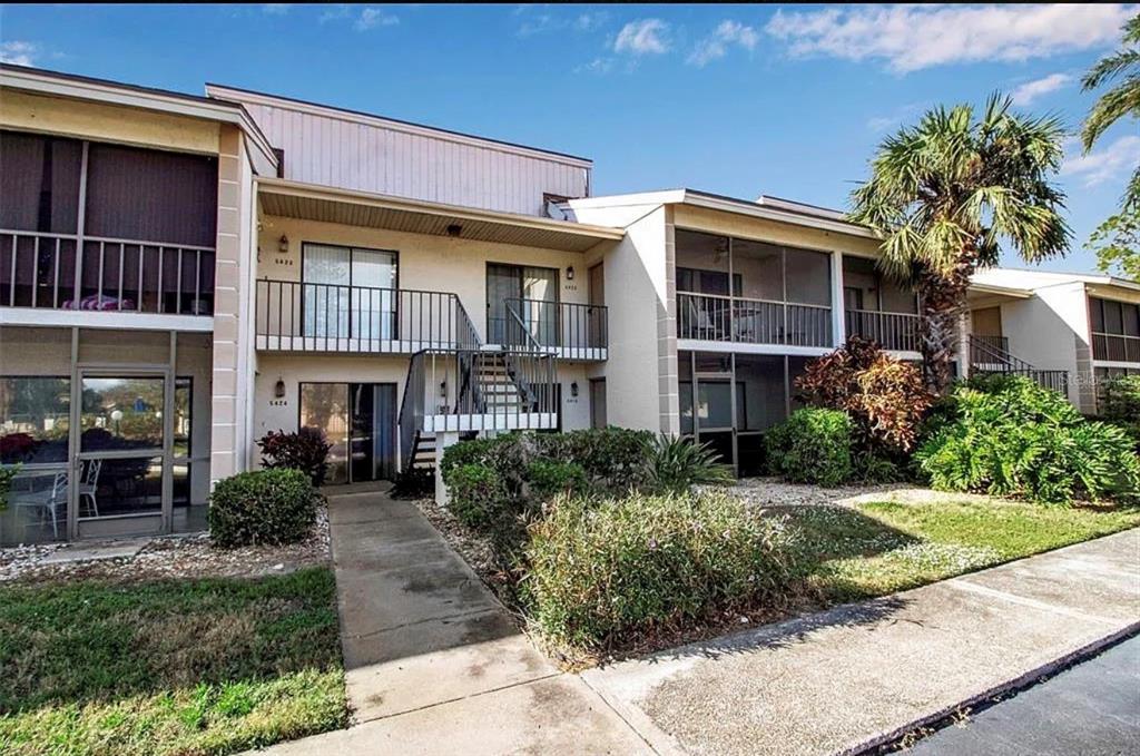 A two-story apartment building features exterior staircases, screened balconies, and landscaped grounds — 5420 SWIFT ROAD UNIT 38, SARASOTA, FL