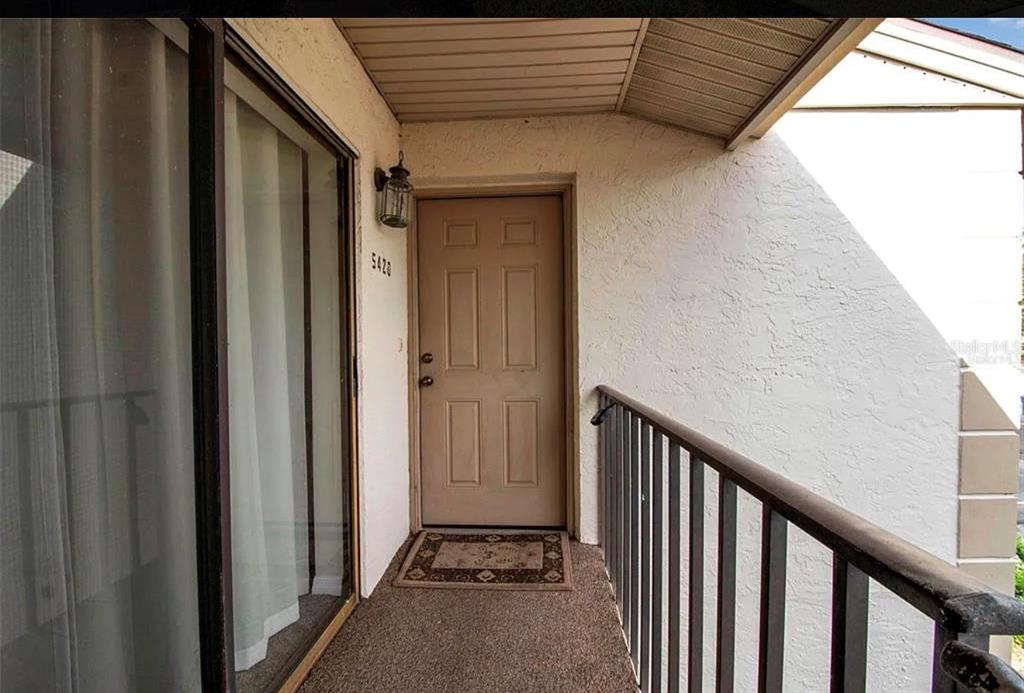 An exterior view of a residential balcony featuring a tan door and sliding glass door — 5420 SWIFT ROAD UNIT 38, SARASOTA, FL