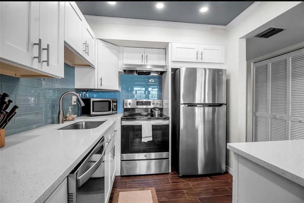 A kitchen features white cabinets, stainless steel appliances, a light blue backsplash, and quartz countertops — 5420 SWIFT ROAD UNIT 38, SARASOTA, FL