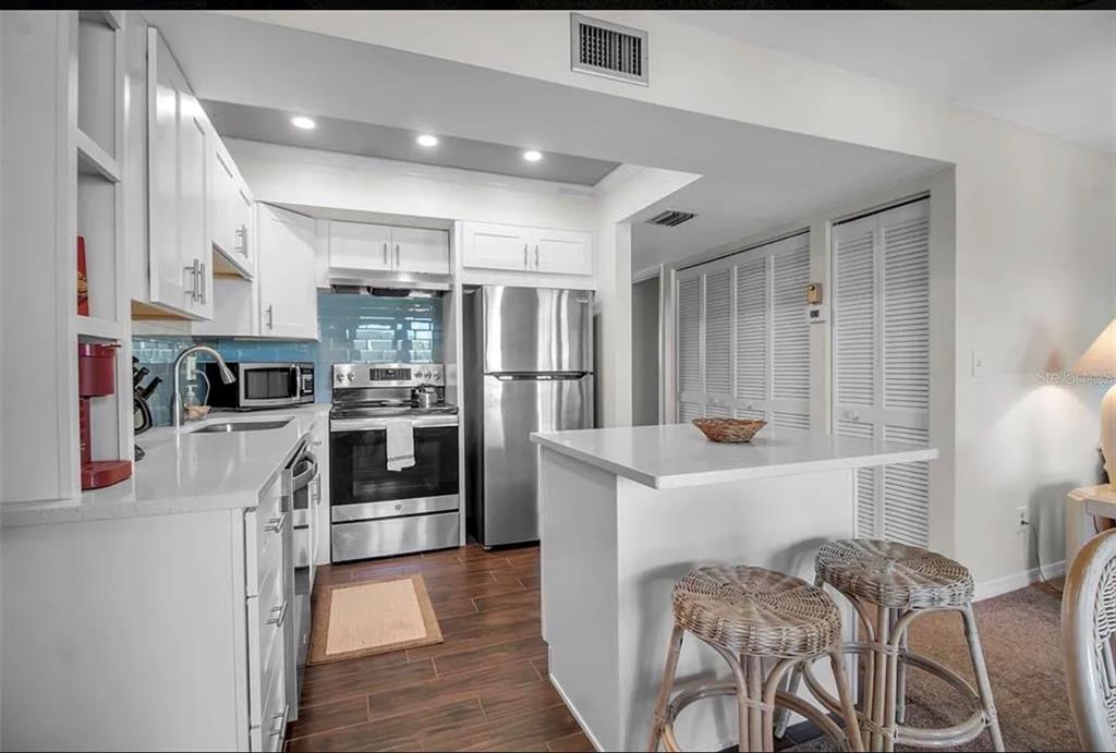 A kitchen features white cabinetry, stainless steel appliances, a small island, and dark wood flooring — 5420 SWIFT ROAD UNIT 38, SARASOTA, FL