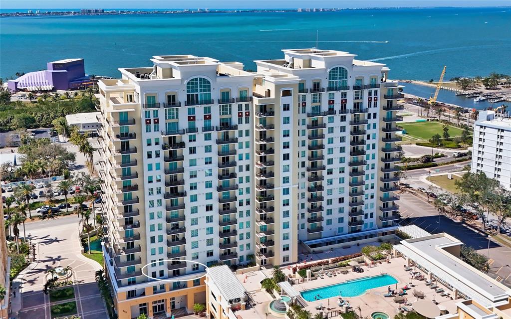 An aerial view shows a large multi-story residential building with a pool and waterfront — 800 N TAMIAMI TRAIL UNIT 312, SARASOTA, FL