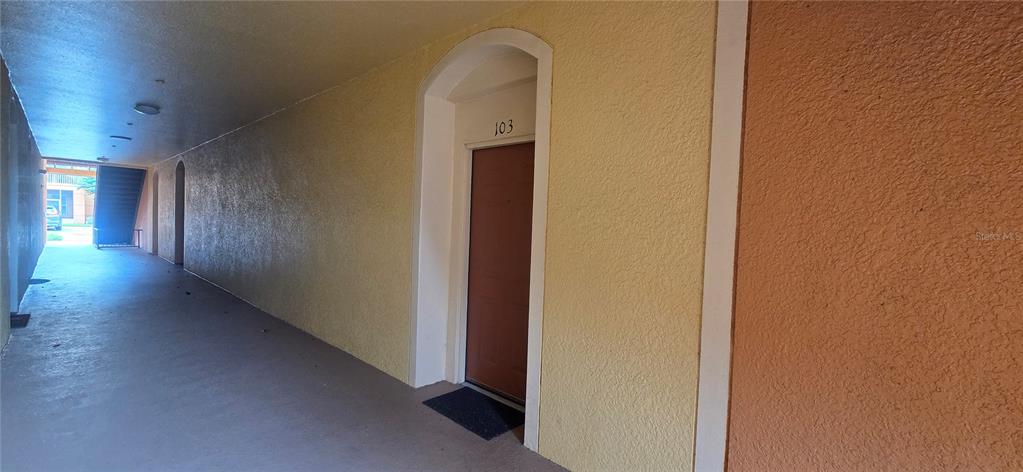 An exterior view of a covered apartment building walkway featuring a brown door labeled 103 — 6240 CONTESSA DRIVE UNIT 103, ORLANDO, FL