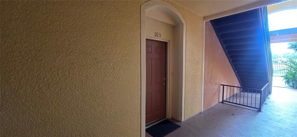 An exterior view of a brown apartment door numbered 103 next to a staircase — 6240 CONTESSA DRIVE UNIT 103, ORLANDO, FL