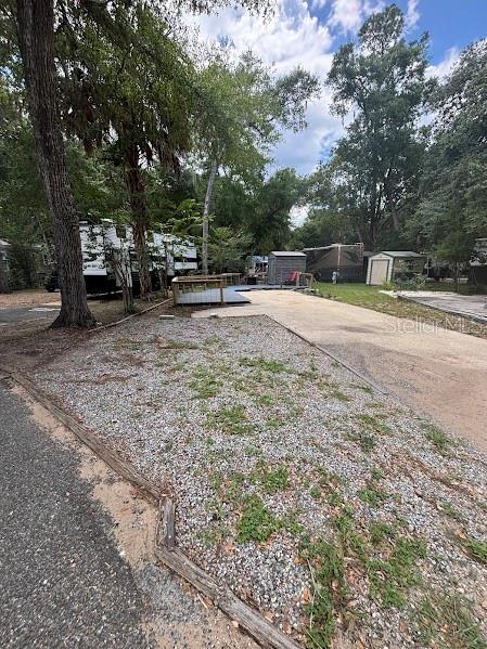 A gravel lot with a wooden deck and a small shed sits among mature trees — 25219 141ST LANE NE UNIT 252, FORT MC COY, FL
