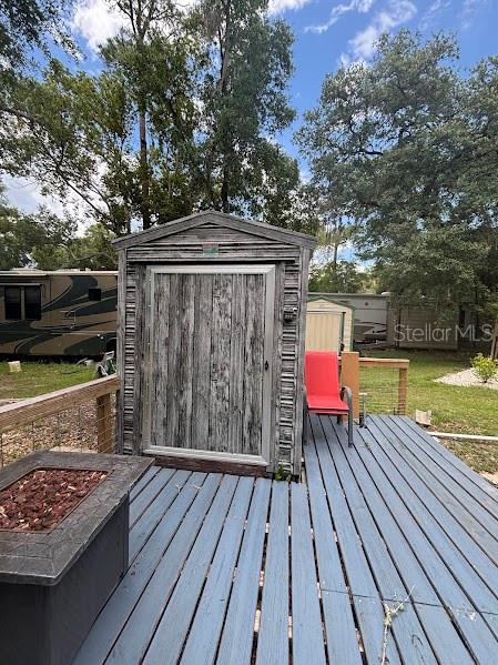 A wooden shed sits on a blue deck next to a fire pit and RV — 25219 141ST LANE NE UNIT 252, FORT MC COY, FL
