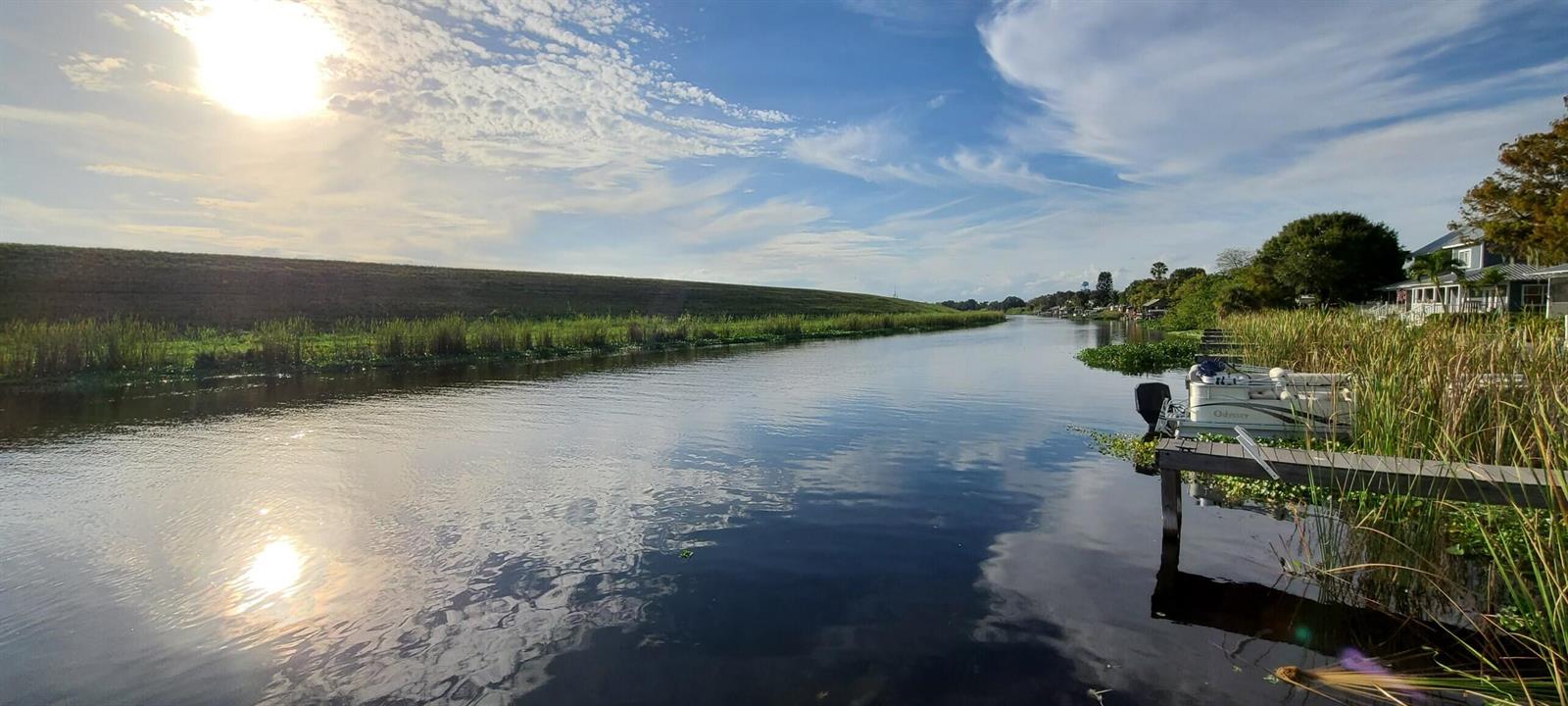 A canal view features a wooden dock, a pontoon boat, and a grassy embankment — 4334 SE Us Highway 441 # 11, Okeechobee FL 34974, OKEECHOBEE, FL