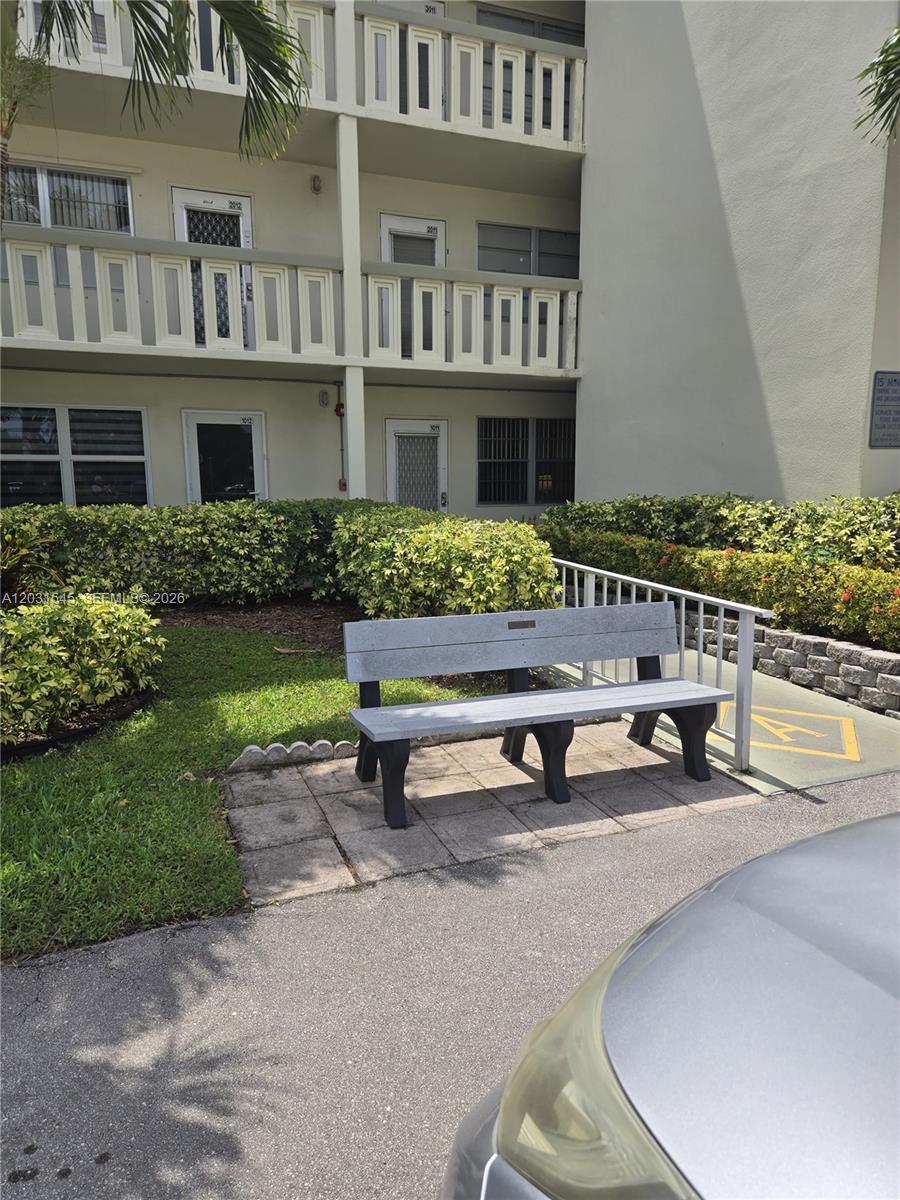 A gray bench sits on a paved patio in front of a multi-story apartment building — DEERFIELD BEACH, FL