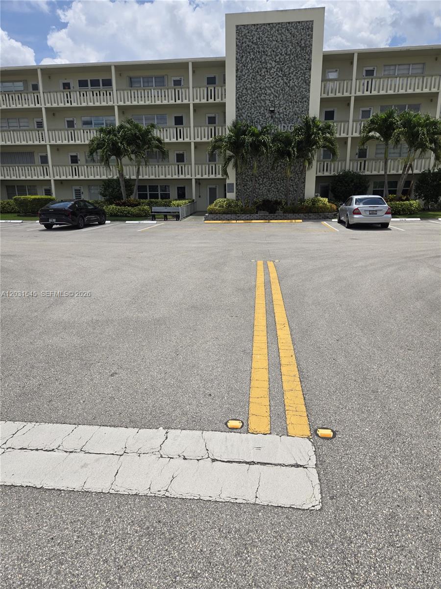 The exterior of a multi-story apartment building features a parking lot with marked spaces — DEERFIELD BEACH, FL