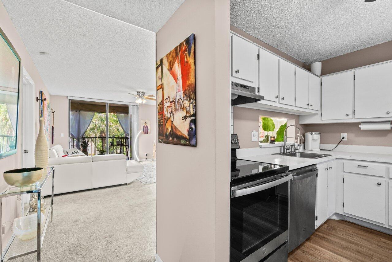 A kitchen with white cabinets and stainless steel appliances opens into a carpeted living area — 5100 Las Verdes Circle # 316, Delray Beach FL 33484, DELRAY BEACH, FL