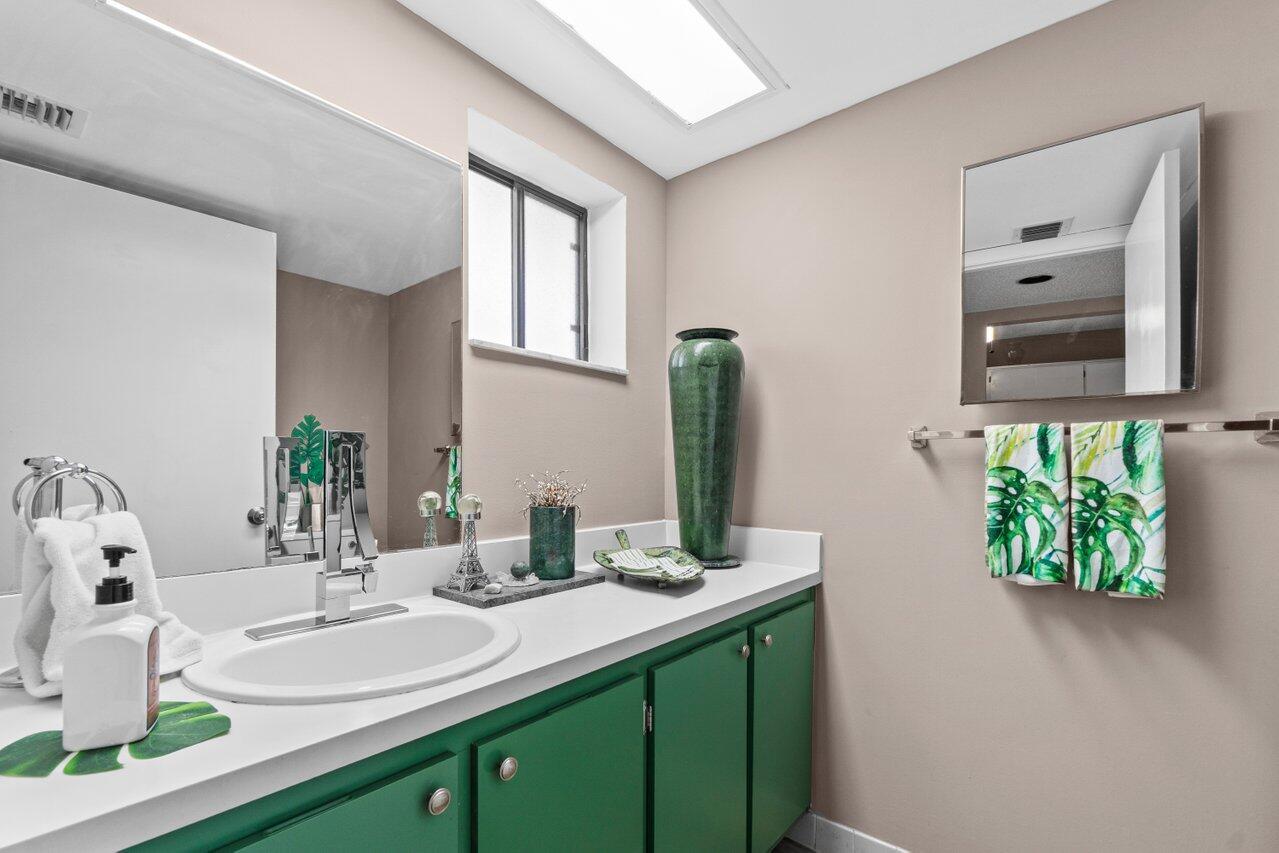 A bathroom features a green vanity, white countertop, large mirror, and tropical-patterned hand towels — 5100 Las Verdes Circle # 316, Delray Beach FL 33484, DELRAY BEACH, FL