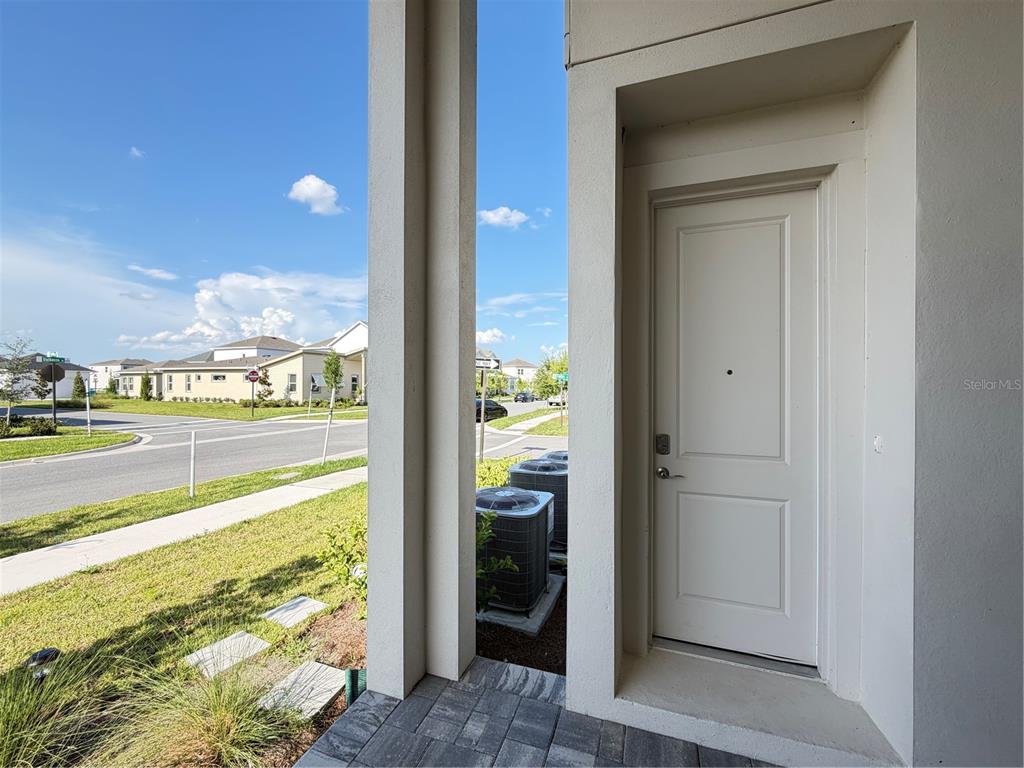 A white exterior door is set into a recessed entryway next to two HVAC units — 10108 FIDDLEY ALY, ORLANDO, FL