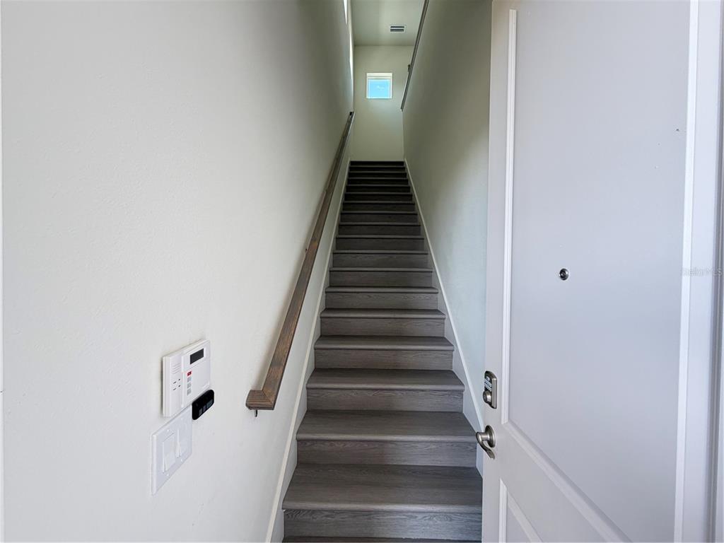 A staircase with dark wood-look treads and a handrail leads upward toward a small window — 10108 FIDDLEY ALY, ORLANDO, FL