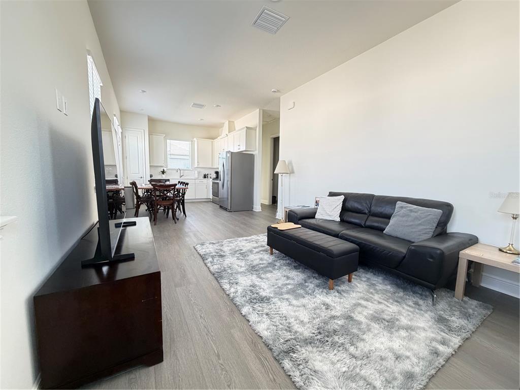 An open-concept living room and kitchen featuring light wood flooring and a black leather sofa — 10108 FIDDLEY ALY, ORLANDO, FL