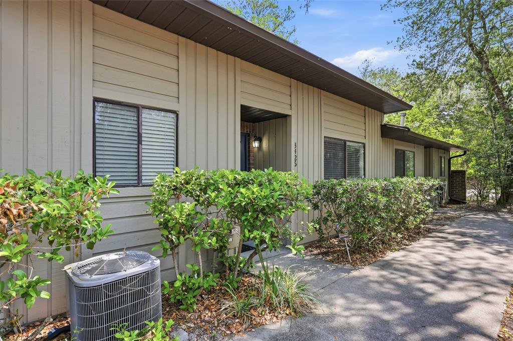 A tan house exterior features vertical siding, a concrete walkway, and an outdoor AC unit — 3426 NW 37TH AVENUE UNIT 3426, GAINESVILLE, FL