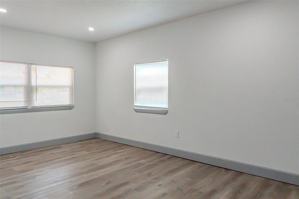 An empty room features white walls, gray baseboards, wood-look flooring, and two windows with blinds — 217 BETTY AVENUE S, DUNDEE, FL