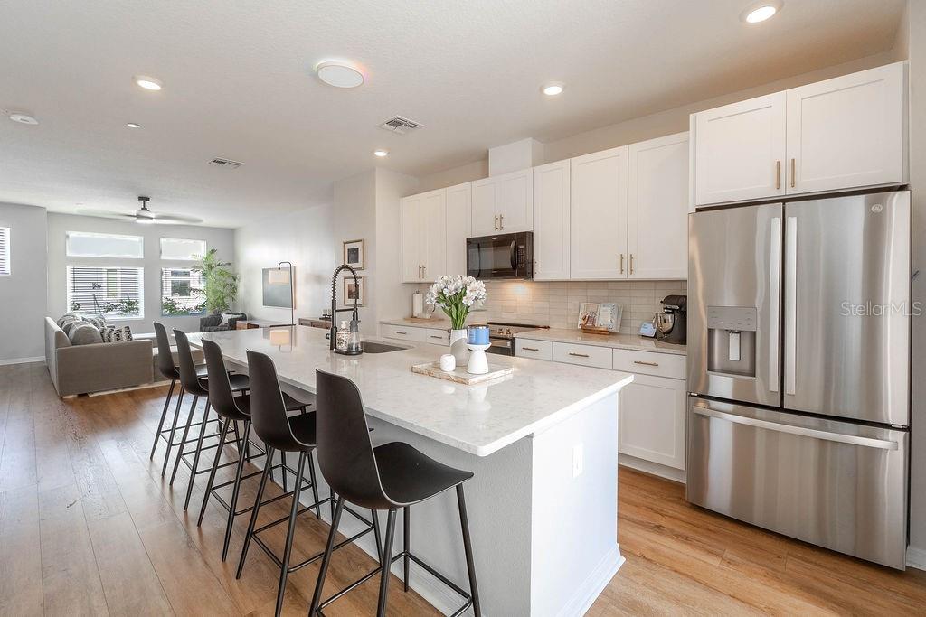 A modern kitchen features white cabinets, a large quartz island with bar stools, and stainless appliances — 12941 GABOR AVENUE, ORLANDO, FL