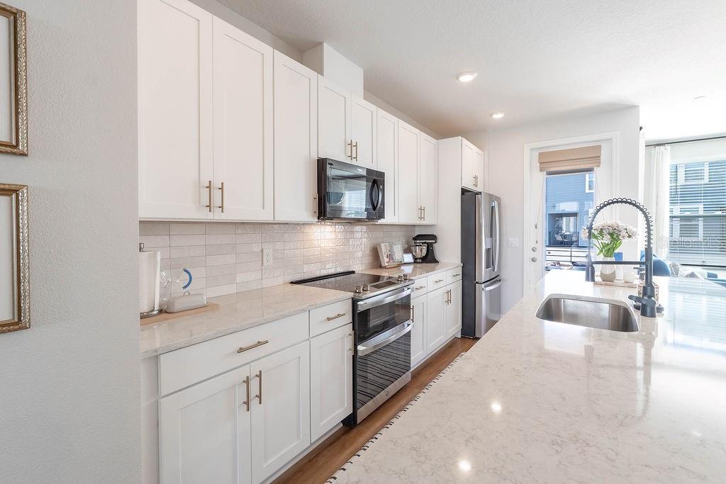 A modern kitchen features white cabinets, quartz countertops, stainless steel appliances, and a large island — 12941 GABOR AVENUE, ORLANDO, FL