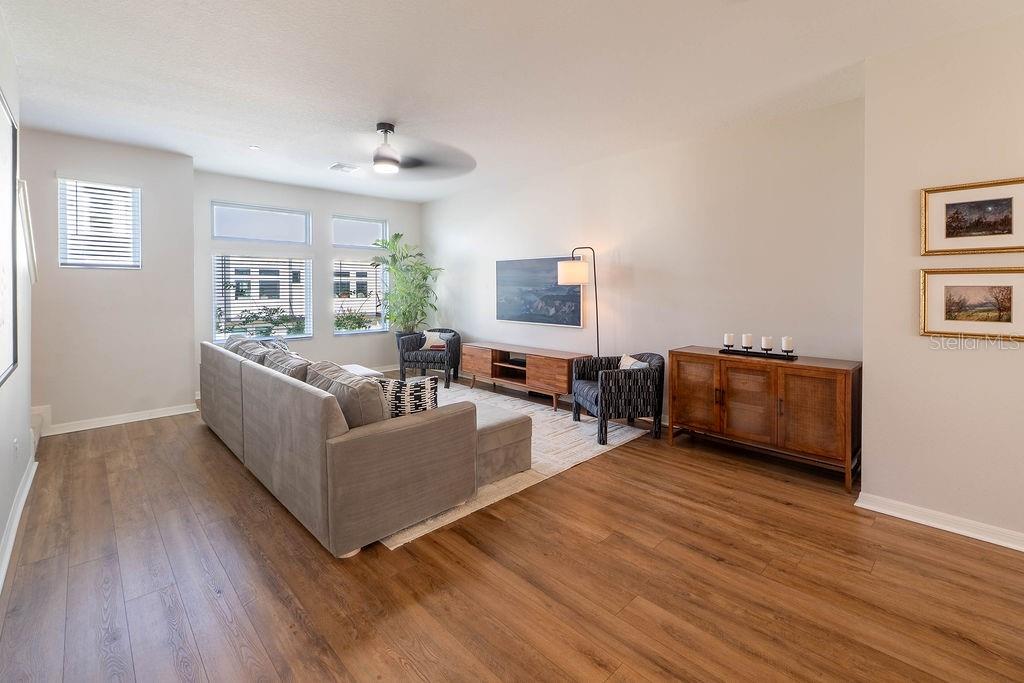 A living room with wood-look flooring, a gray sectional sofa, and a wooden media console — 12941 GABOR AVENUE, ORLANDO, FL