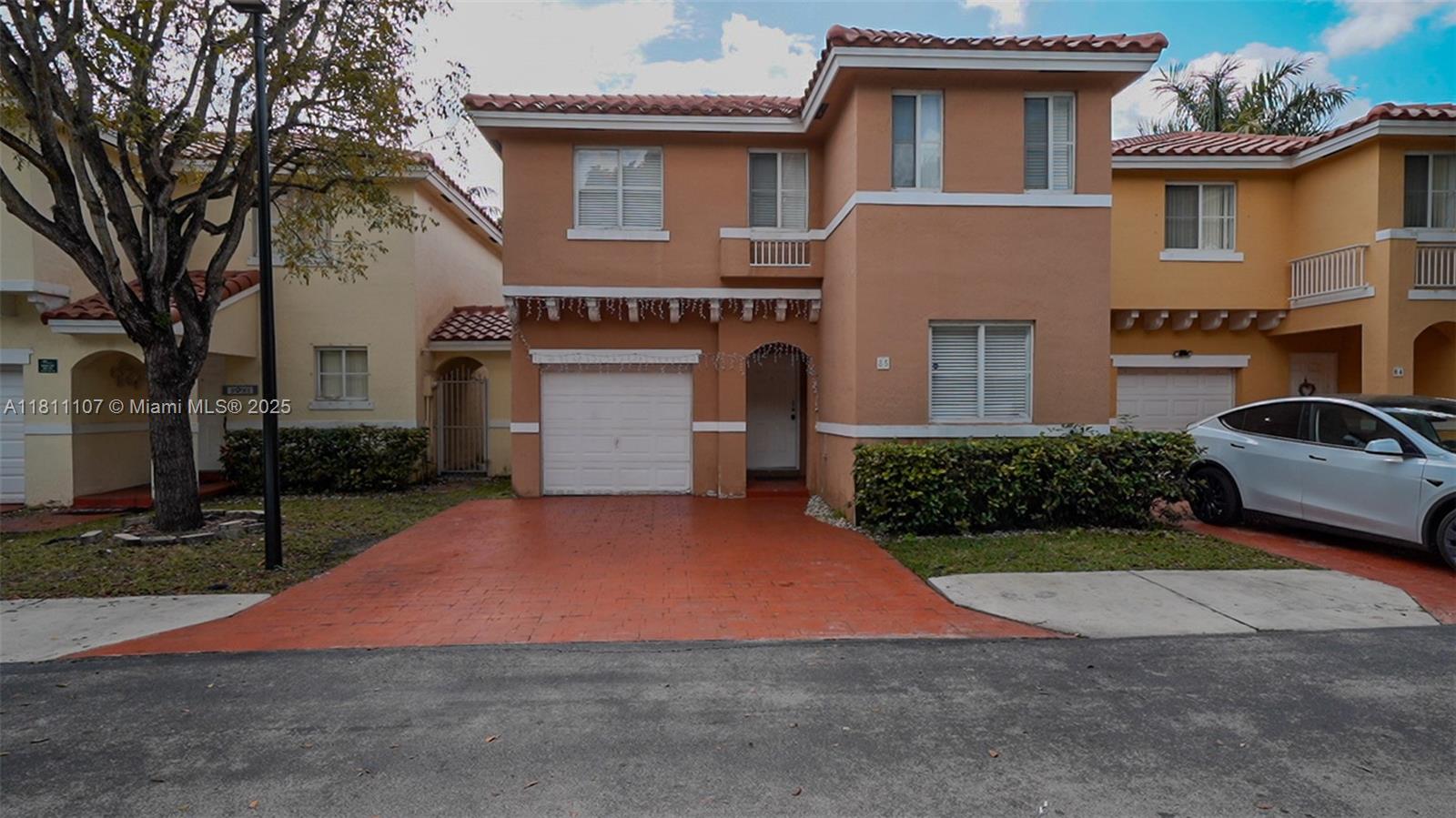 A two-story stucco townhouse features a terracotta-tiled roof, a white garage door, and a driveway — 14816 SW 104th St # 85, Miami FL 33196, MIAMI, FL