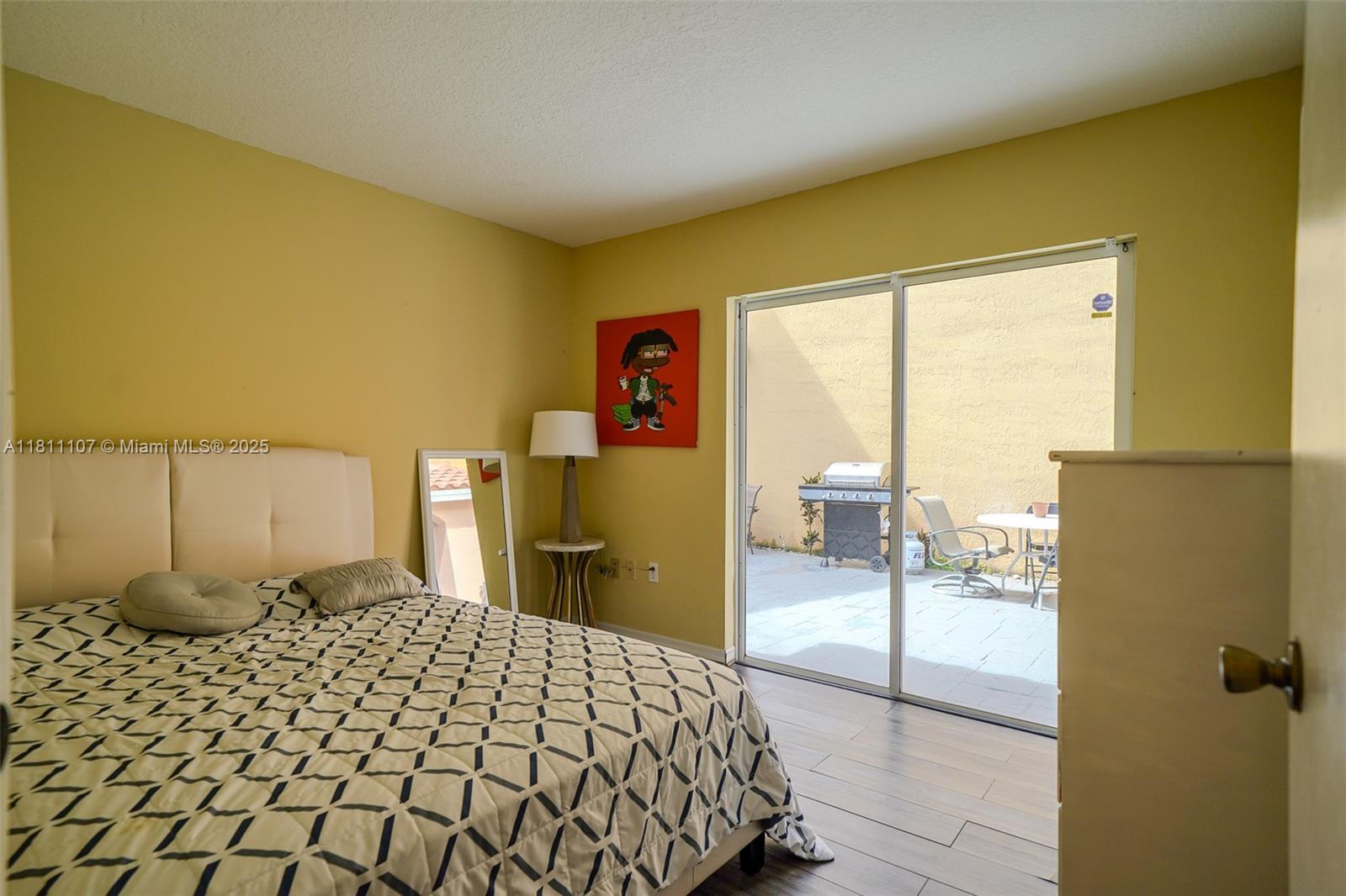 A bedroom features a bed, yellow walls, a sliding glass door, and an outdoor patio — 14816 SW 104th St # 85, Miami FL 33196, MIAMI, FL