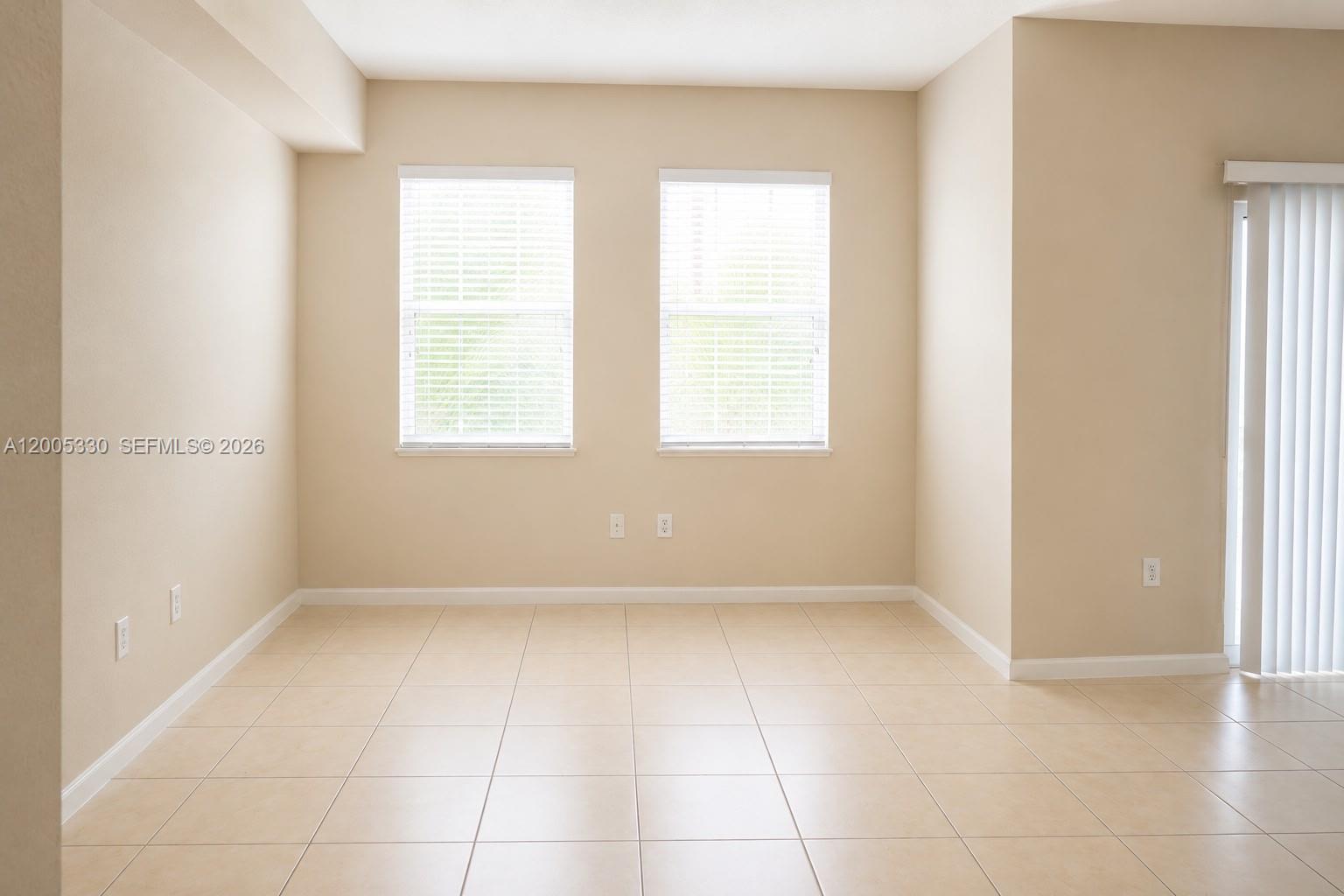 An empty room features beige walls, tiled flooring, two windows with blinds, and a sliding door — 11503 NW 89th St # 213, Doral FL 33178, DORAL, FL