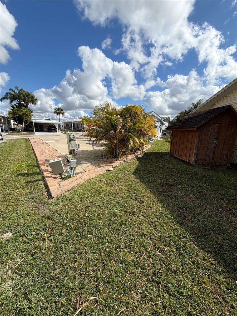 A grassy yard features a brick-bordered driveway, a palm tree, and a small wooden shed — 6614 SE 53rd Lane, Okeechobee FL 34974, OKEECHOBEE, FL
