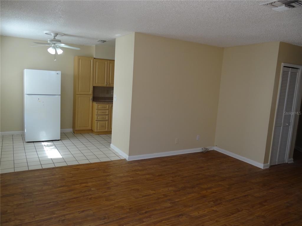 An open-concept room features wood-look flooring, a tiled kitchen area, and a white refrigerator — 2983 62ND AVENUE N, ST PETERSBURG, FL