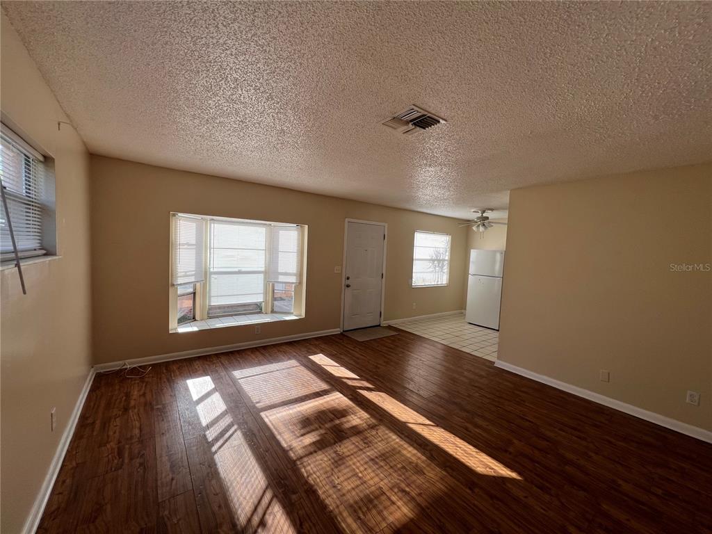 An open living area features wood-look flooring, a bay window, and an adjacent kitchen space — 2983 62ND AVENUE N, ST PETERSBURG, FL