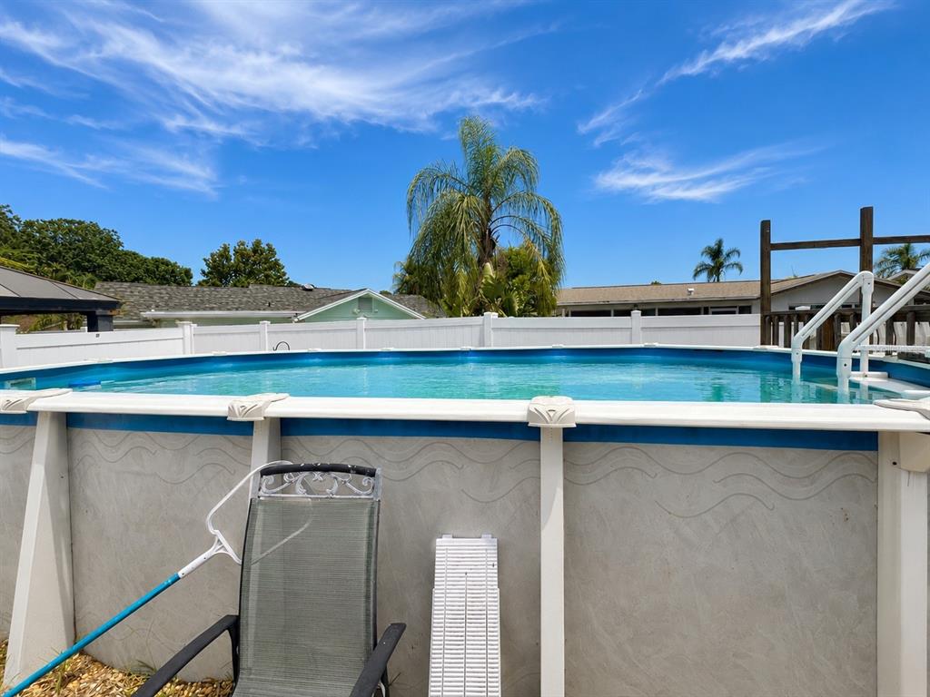An above-ground swimming pool sits in a backyard with a white fence and palm tree — 6834 GREENWICH AVENUE, NEW PORT RICHEY, FL
