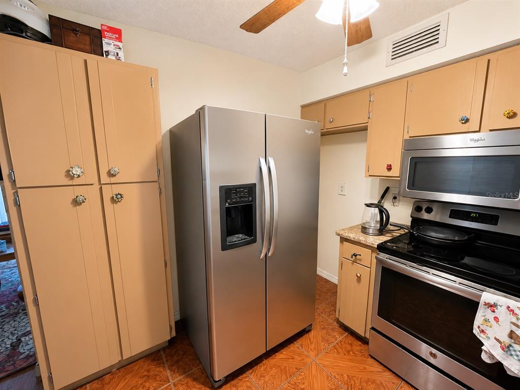 A kitchen features light wood cabinets, stainless steel appliances, and brown tiled flooring — 6834 GREENWICH AVENUE, NEW PORT RICHEY, FL