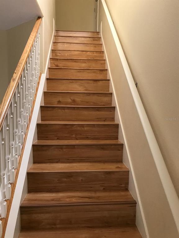 A straight wooden staircase with white railings leads upward toward a landing — 6628 BOUGANVILLEA CRESCENT DRIVE, ORLANDO, FL
