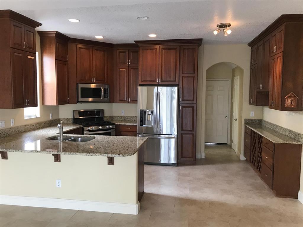 A kitchen features dark wood cabinets, stainless steel appliances, and granite countertops — 6628 BOUGANVILLEA CRESCENT DRIVE, ORLANDO, FL