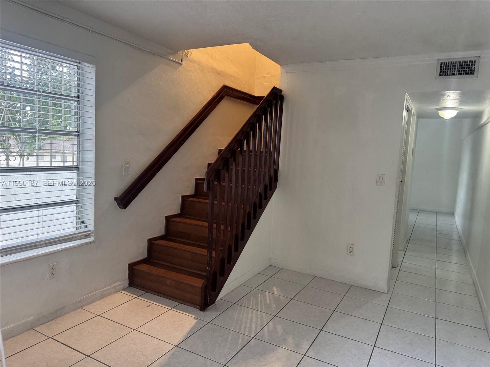 A room with white tiled floors, white walls, and a wooden staircase with a railing — 11 SW 32nd Ave # 4, Miami FL 33135, MIAMI, FL