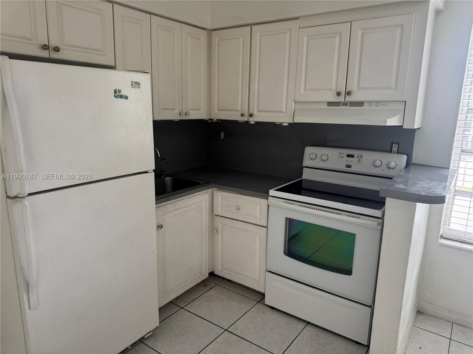 A small kitchen features white cabinets, a white refrigerator, a stove, and tiled flooring — 11 SW 32nd Ave # 4, Miami FL 33135, MIAMI, FL
